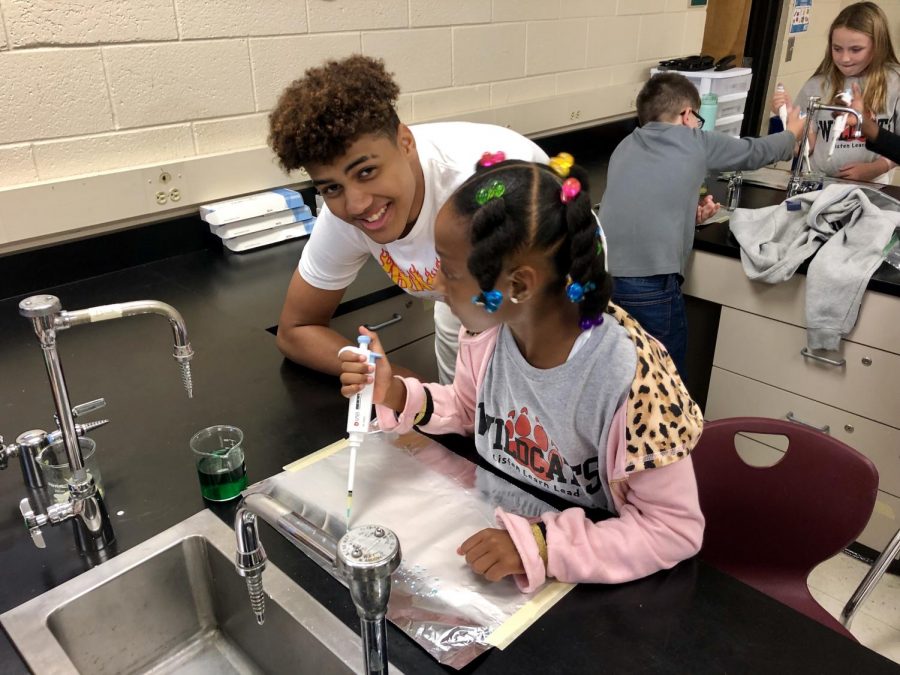 Cedric Arline Jr. is helping an elementary school student pipette her name on foil.