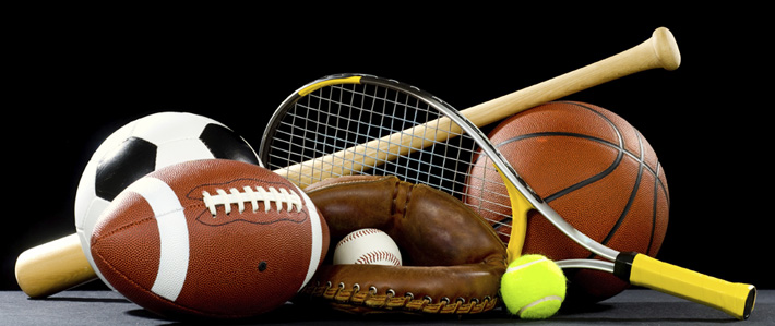 A variety of sports equipment on a black background including an american football, a soccer ball, a baseball, a baseball bat, a tennis raquet, a tennis ball, and a basketball